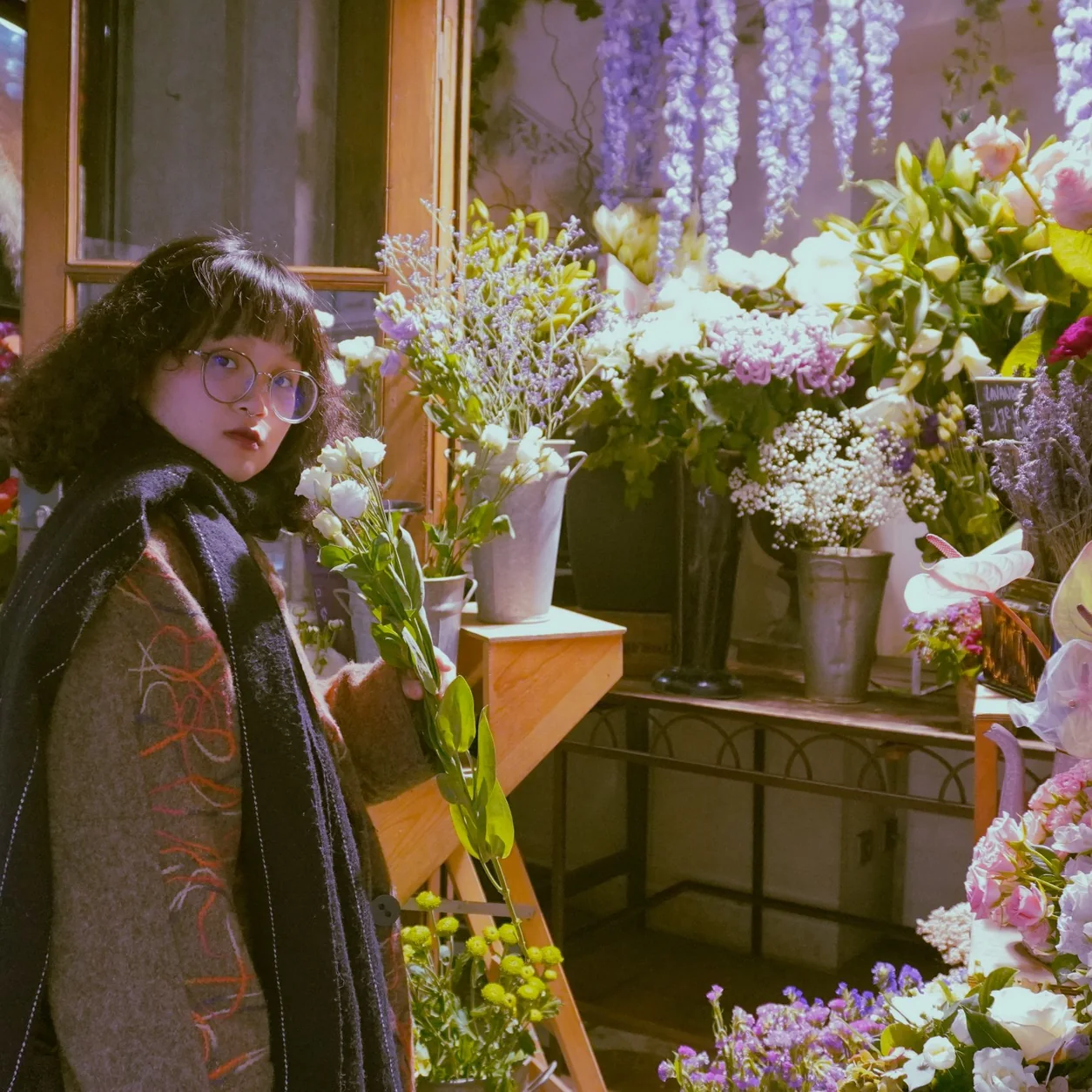 Woman in a florist shop in Lyon surrounded by diverse vibrant floral arrangements.