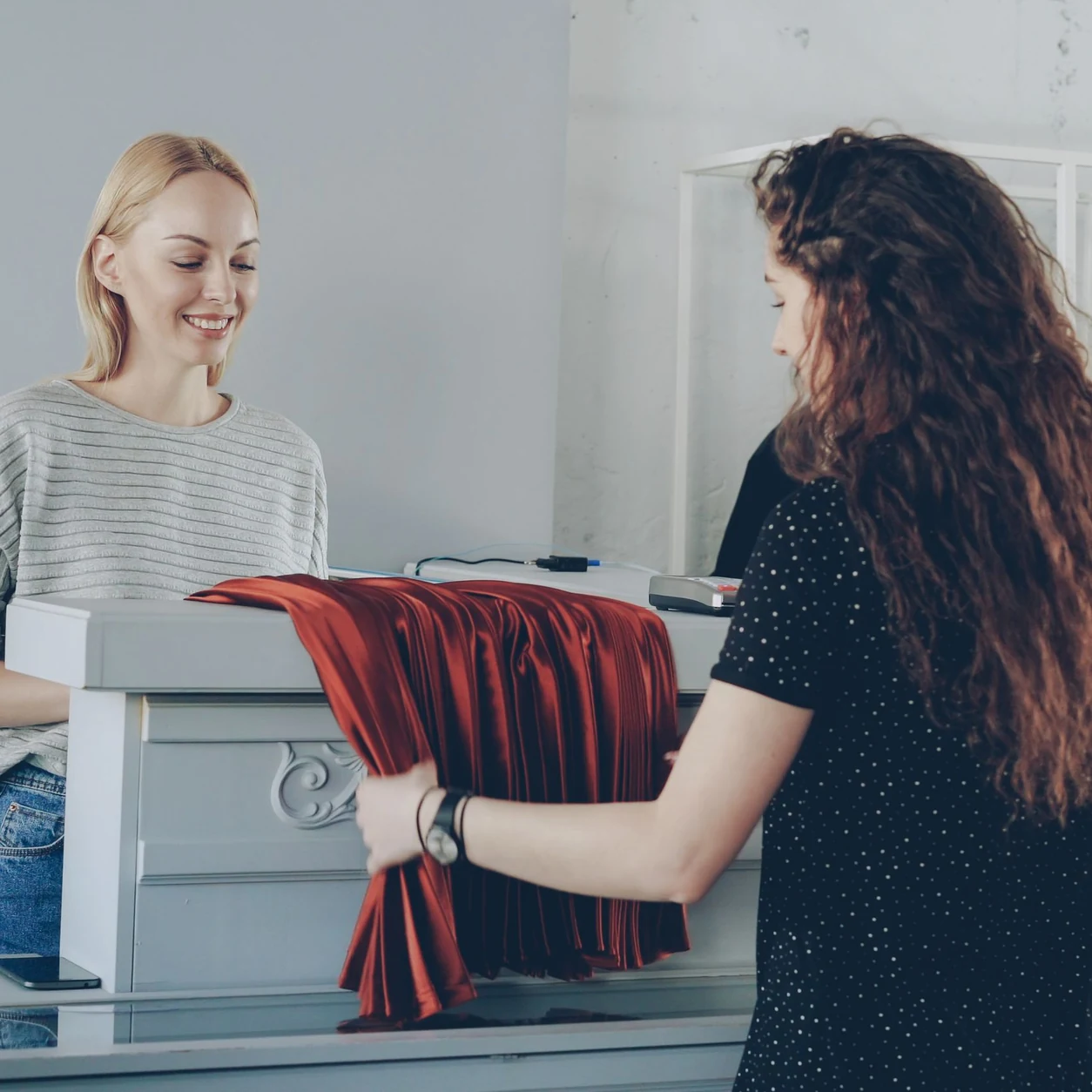 A retail associate and customer talk across the counter of a bright clothing boutique.