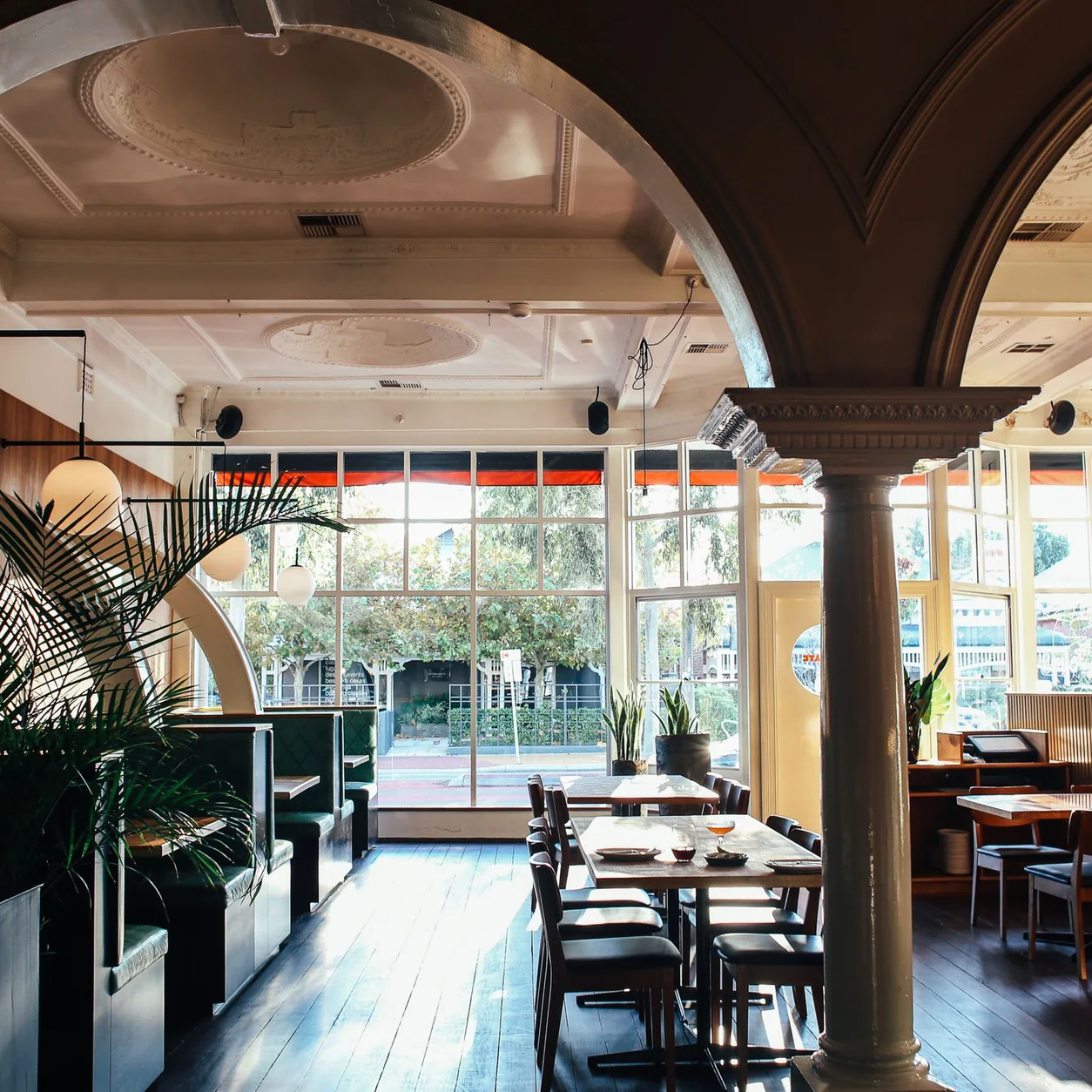 A light-filled restaurant with arches, wood floors and plants.