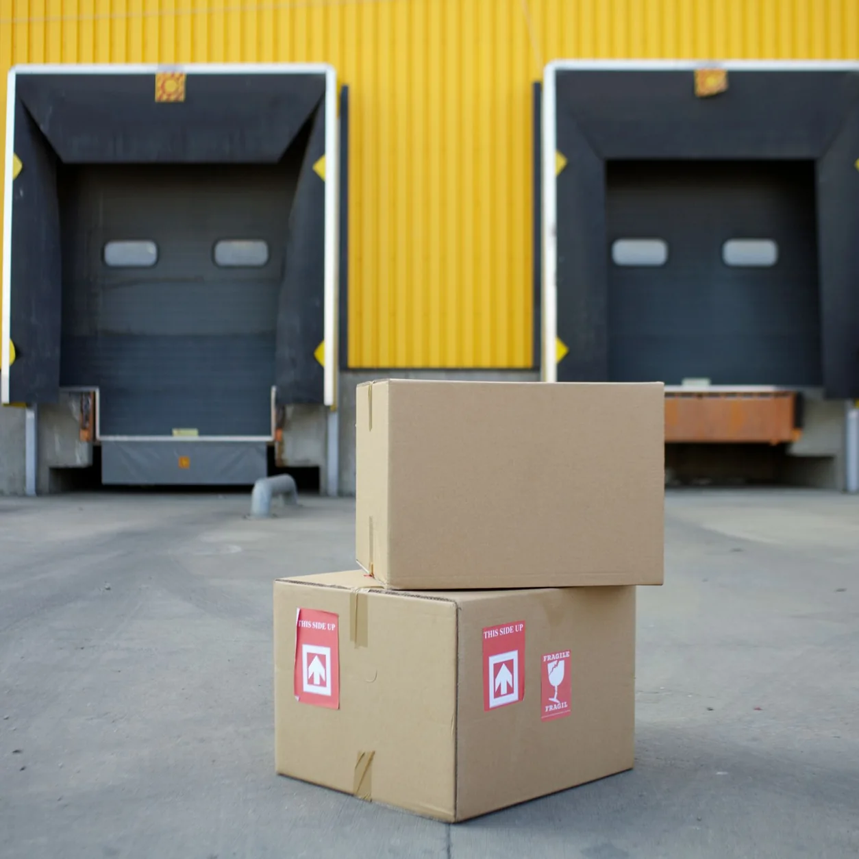 Cartons staged outside yellow warehouse loading doors.