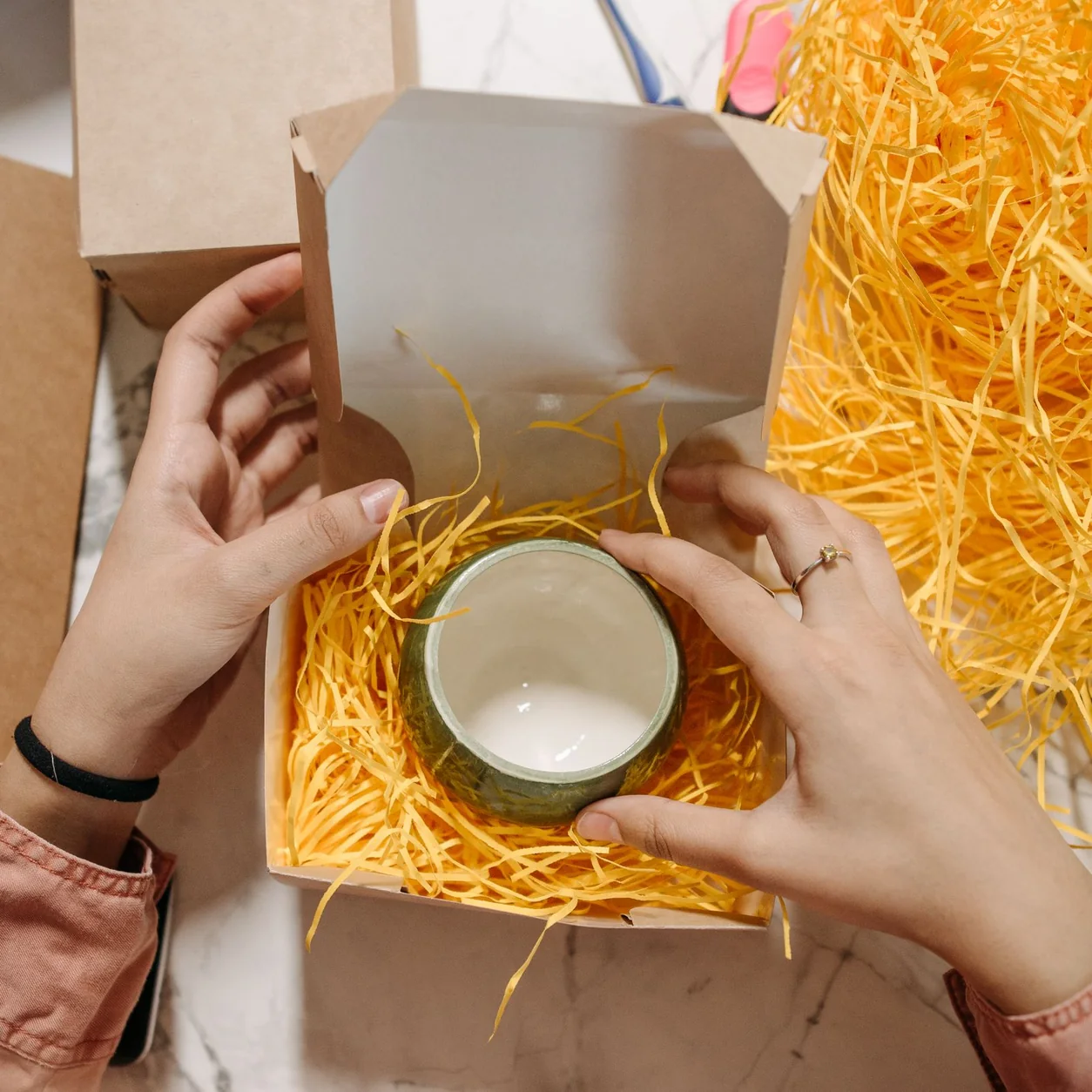 A ceramic cup packed in shredded paper inside a cardboard box.