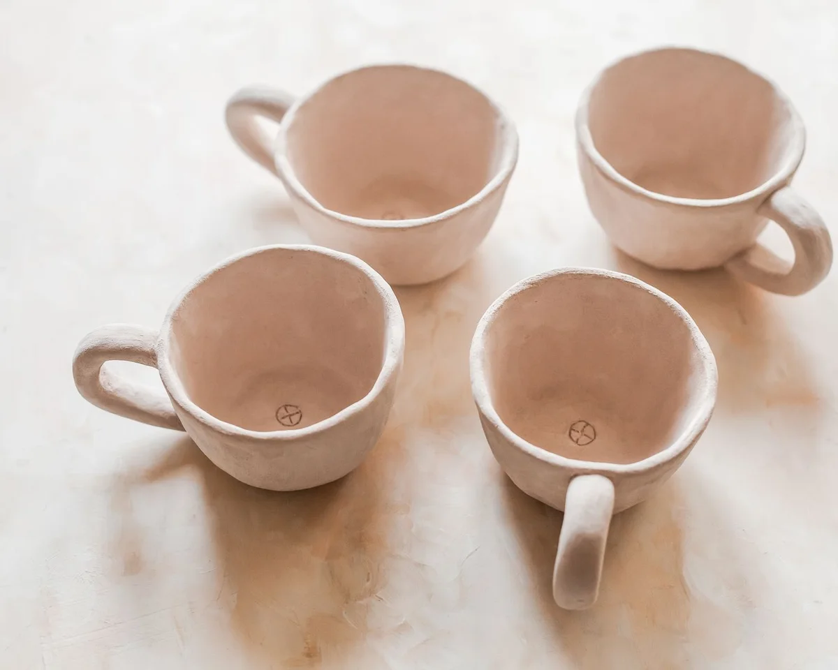 Four handmade ceramic mugs on a pale surface.
