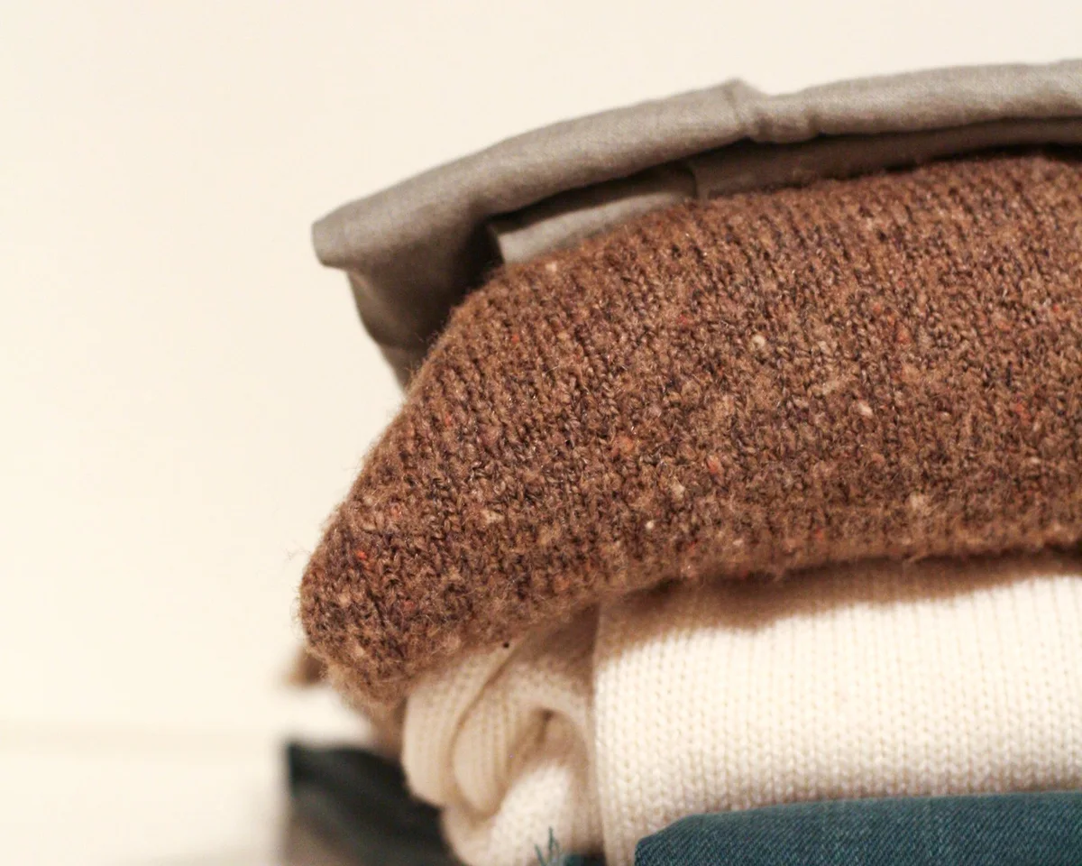 Folded knitwear in warm neutral shades on a white surface.