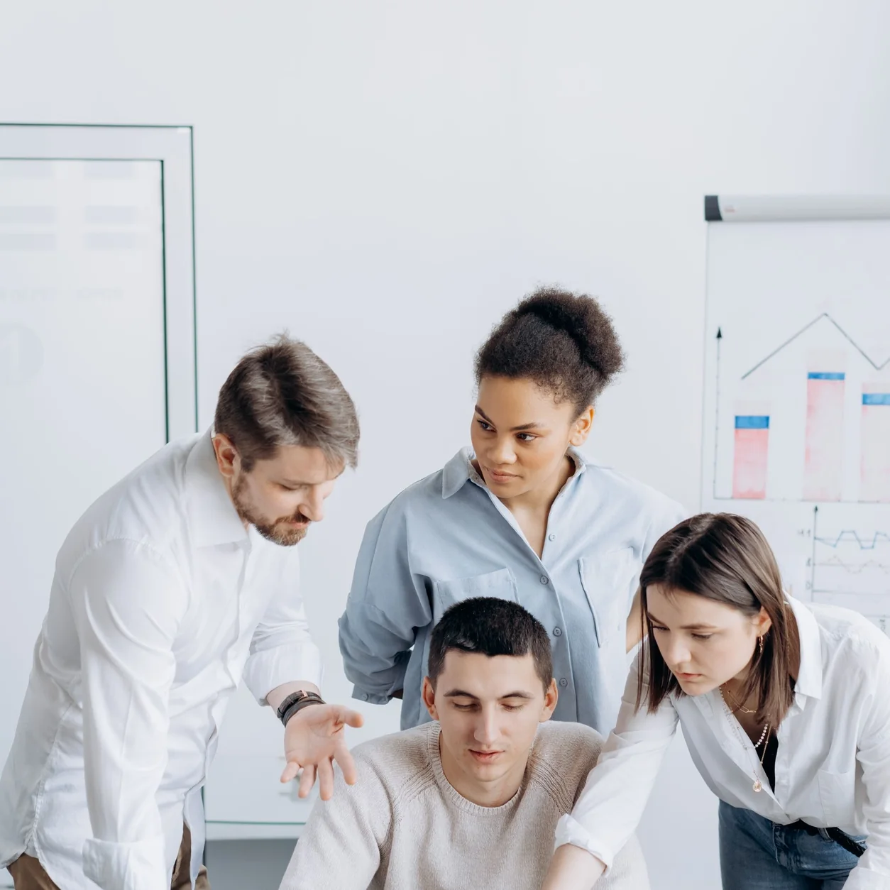 A diverse group of coworkers gathered around a laptop discussing an office project.