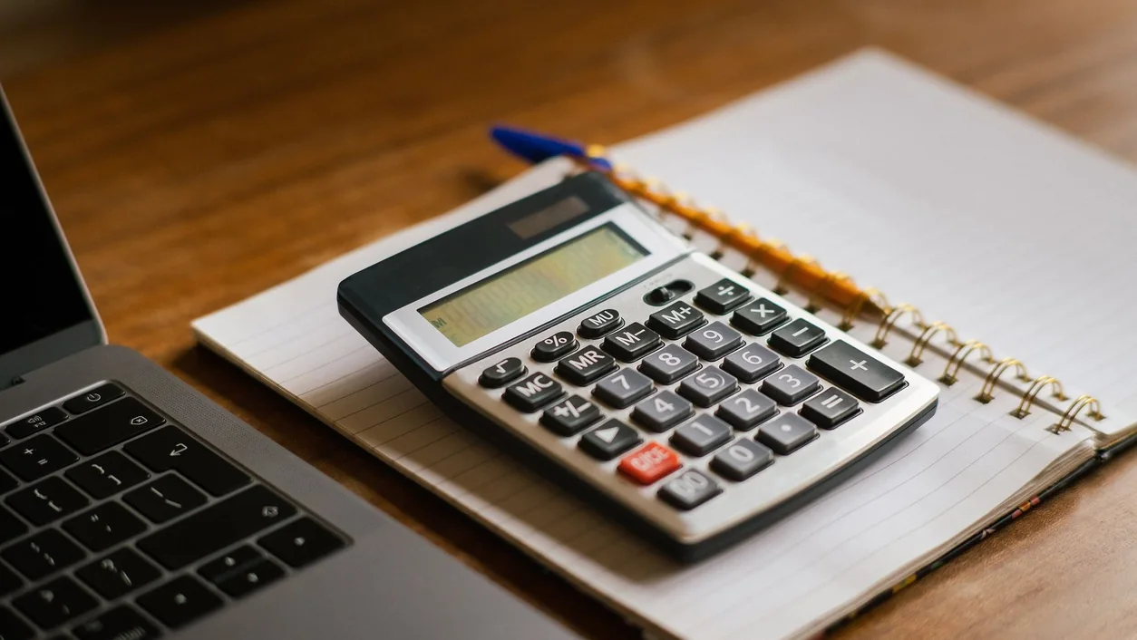 Calculator and open laptop on wooden desk