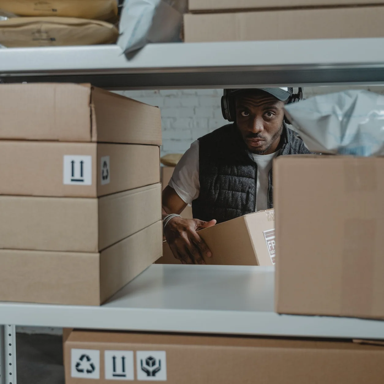 Man organizing packages on shelves in a warehouse setting with cardboard boxes.