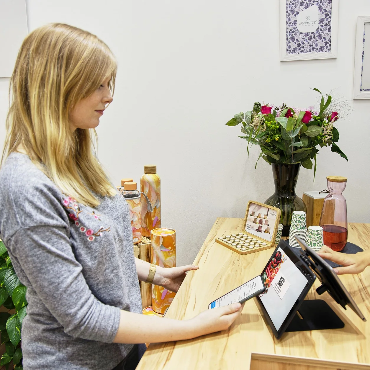 A customer and shopkeeper at a bright retail counter with a tablet.