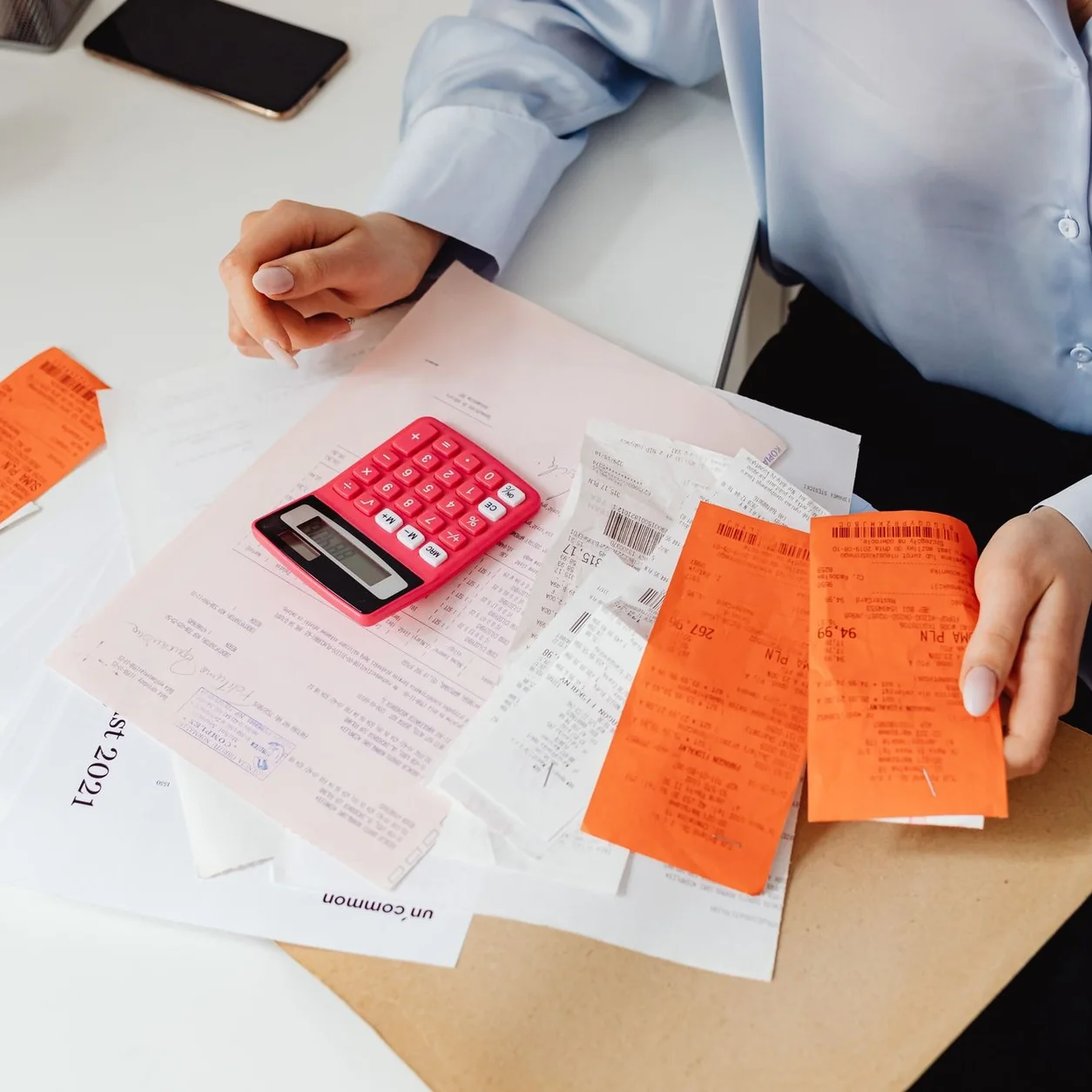 A woman reviews receipts and calculates expenses at a desk with a pink calculator.