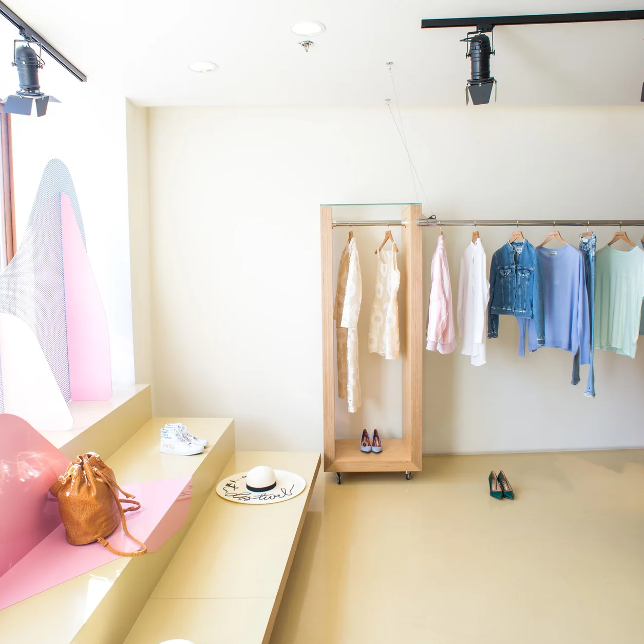 Sunlit fashion boutique with pastel clothing, timber rails and a hat display.