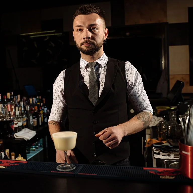 Professional bartender in a stylish lounge bar serving a creamy cocktail with confidence and charisma.