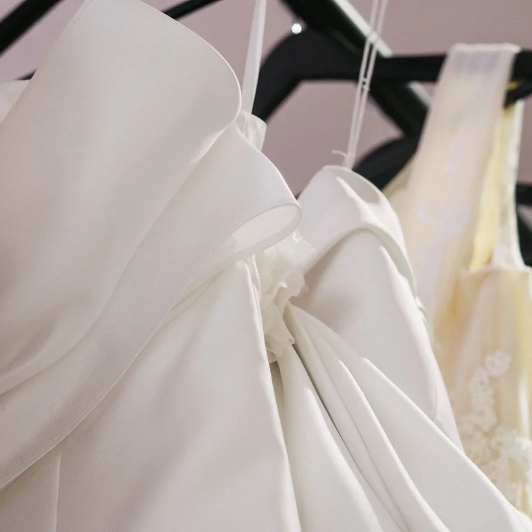 Close-up of elegant wedding gowns hanging in a bridal shop, showcasing intricate details and fabric.