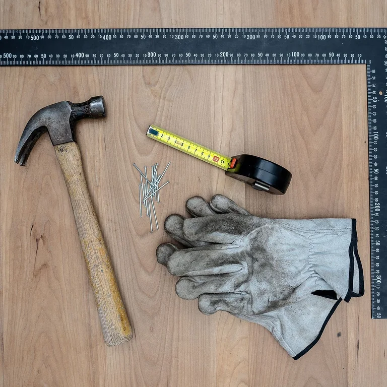 Flat lay of essential carpentry tools including a hammer, gloves, and more on a wooden surface.