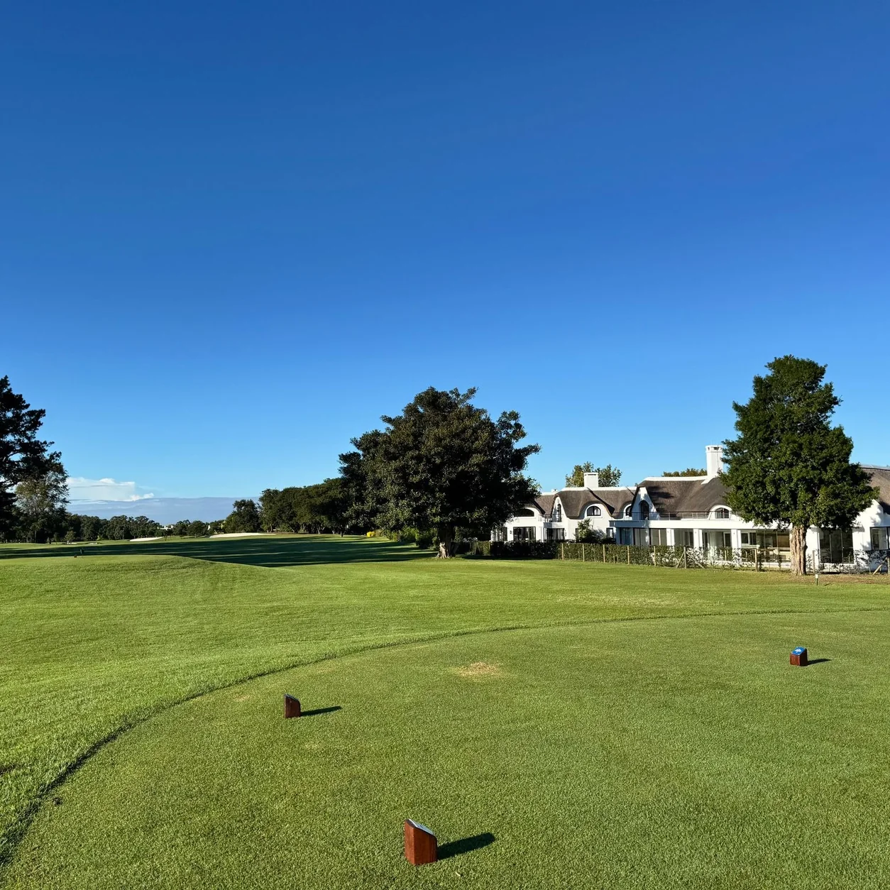 A picturesque view of a golf course fairway with a clubhouse and lush greenery under a clear blue sky.