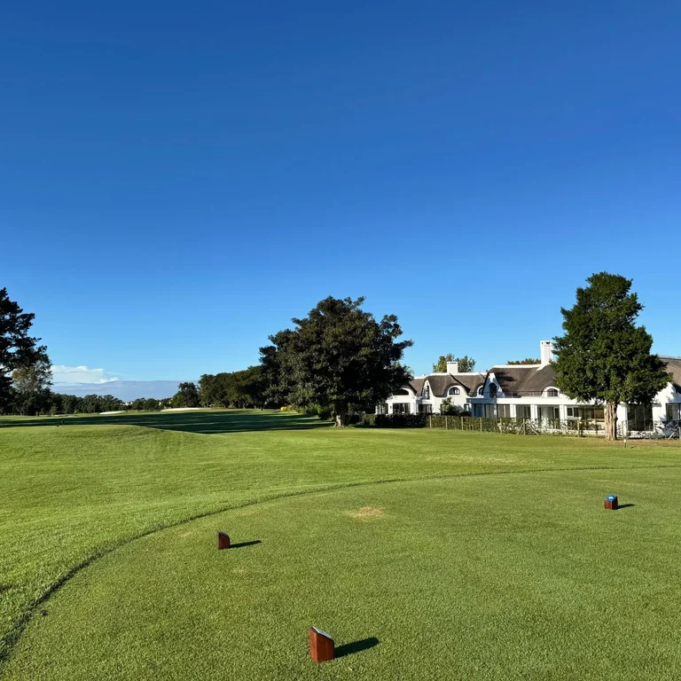 A picturesque view of a golf course fairway with a clubhouse and lush greenery under a clear blue sky.