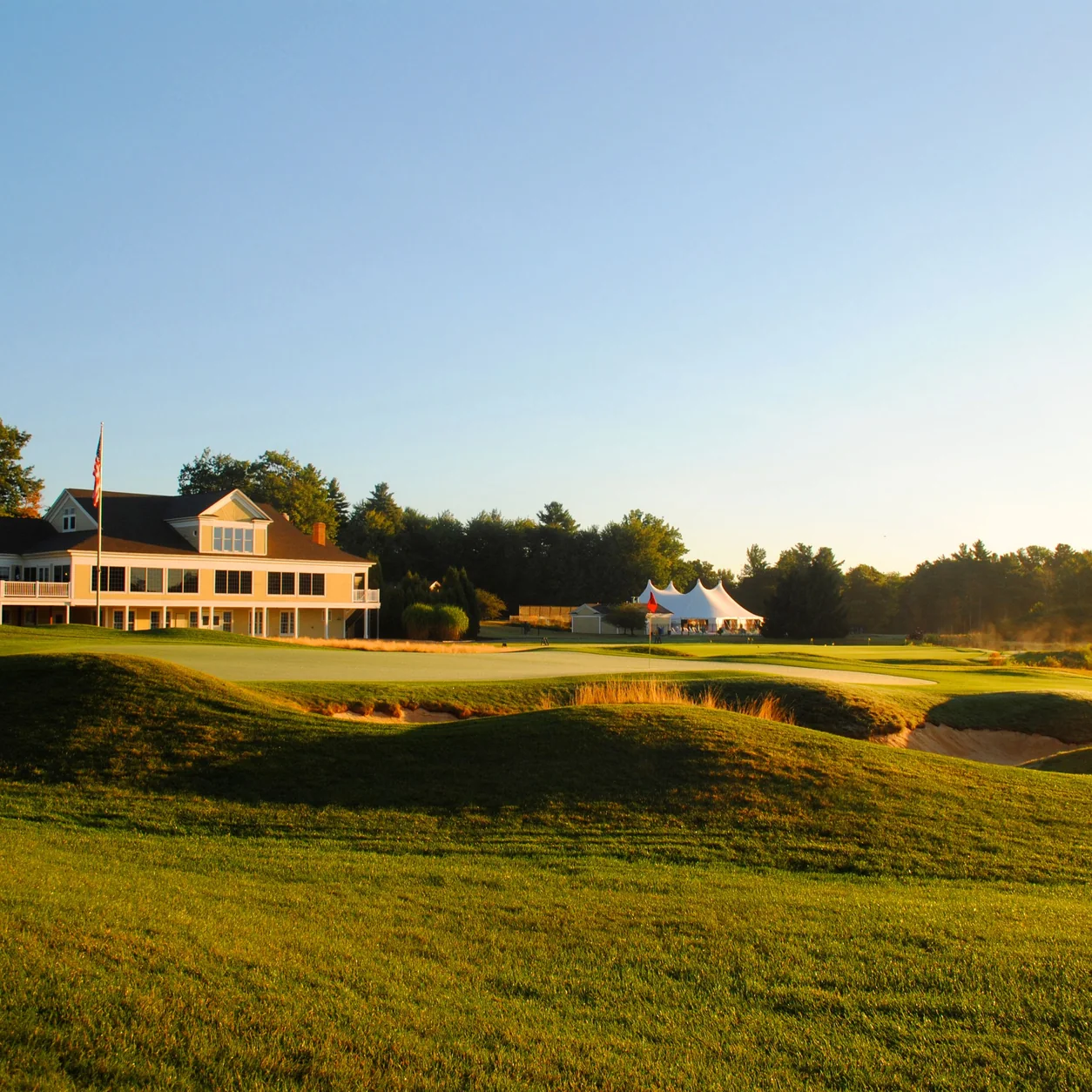 Exterior of typical house located on well groomed golf course surrounded by lush green trees against cloudless blue sky on country club in Falmouth
