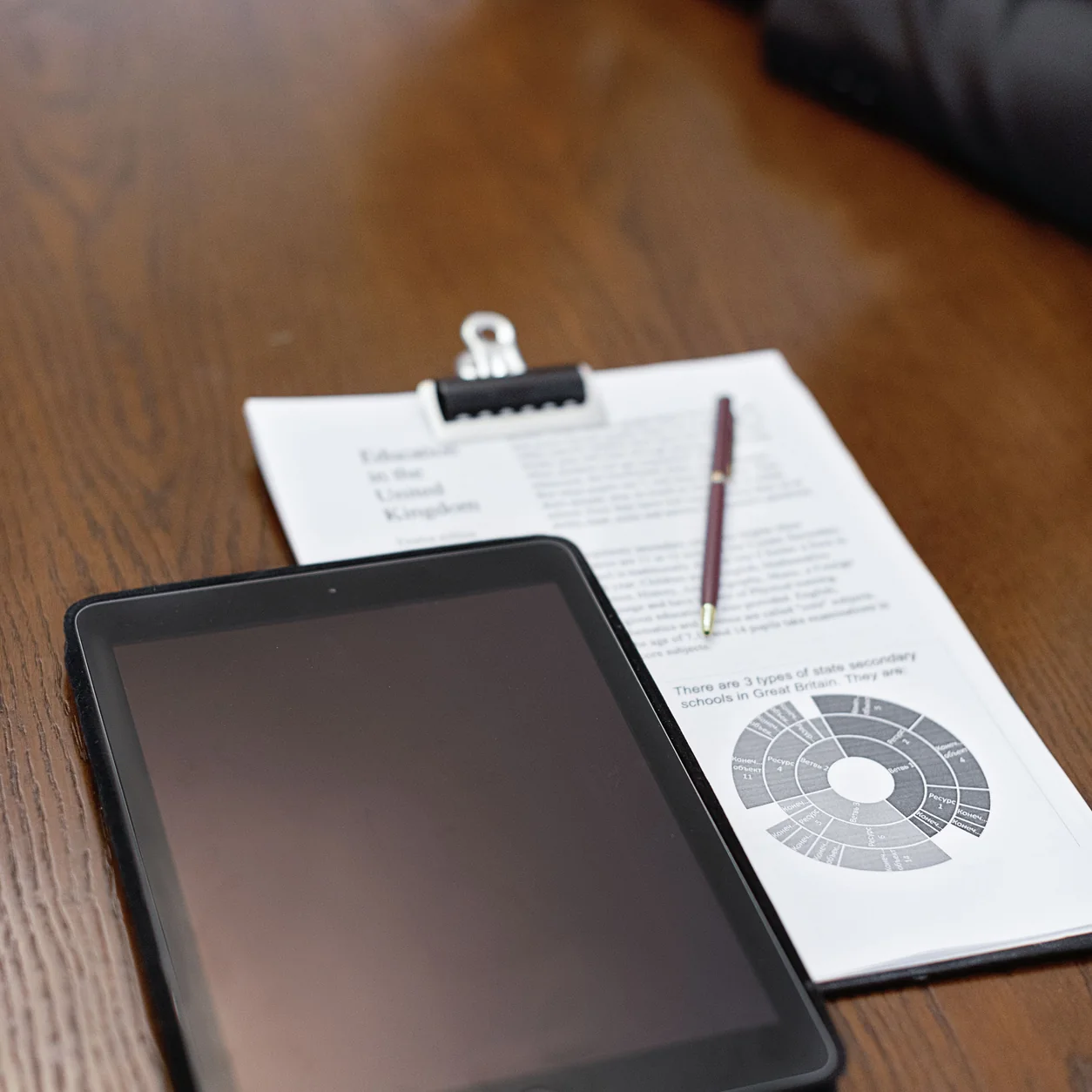 A tablet, documents and pen on a wooden meeting table.