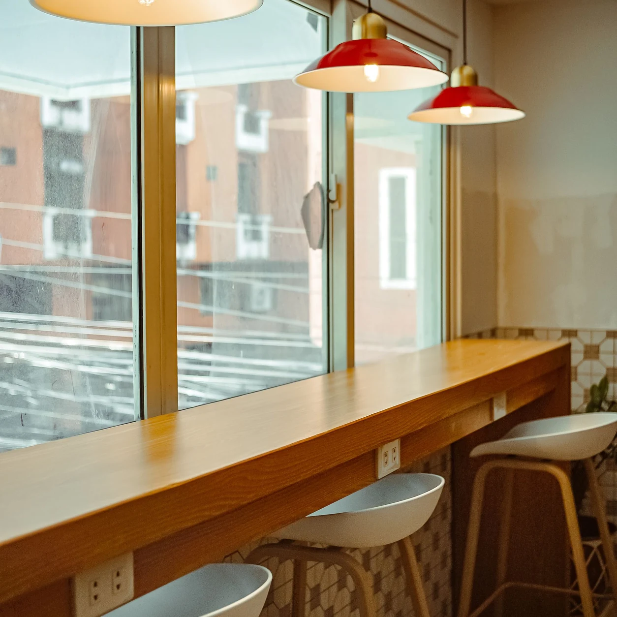 A sunlit café with a polished timber counter, cream stools and warm red pendant lights.