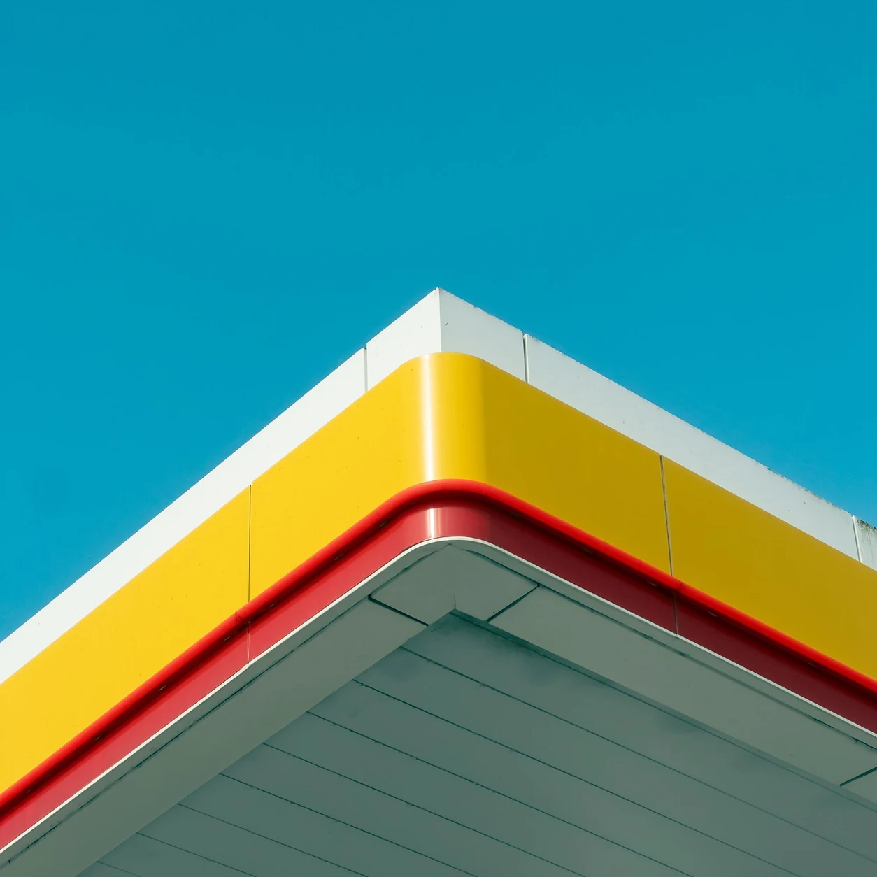 The clean geometric lines of a yellow and red fuel-station canopy against a vivid blue sky.