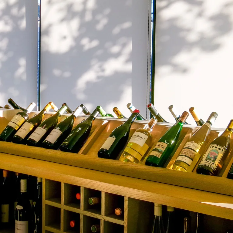 An inviting display of various wine bottles in a modern shop setting, illuminated by natural light.
