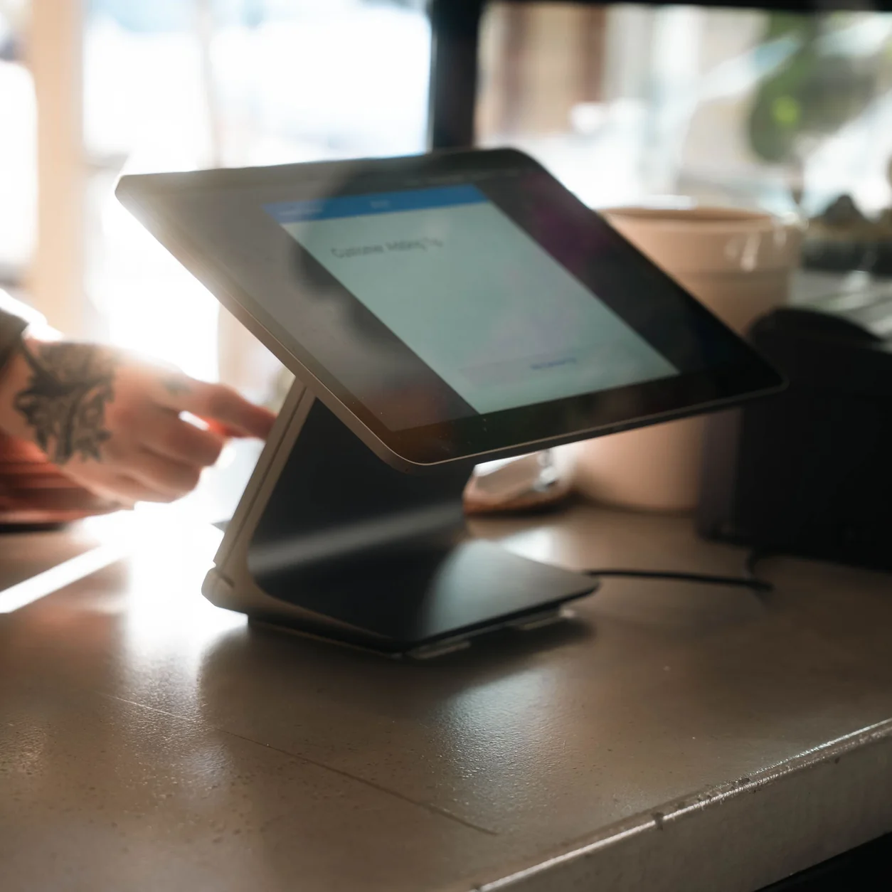 A person using a tablet register on a wooden coffee-shop counter.