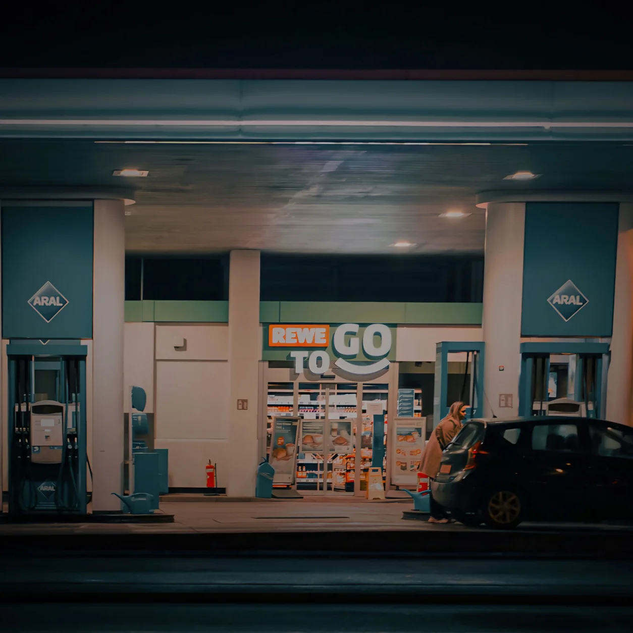 A nighttime view of a gas station and convenience store with a car parked at the pump.