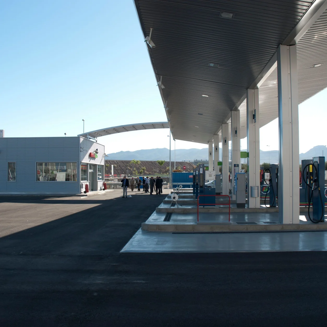 A contemporary fuel station with mountains behind it under a blue sky.