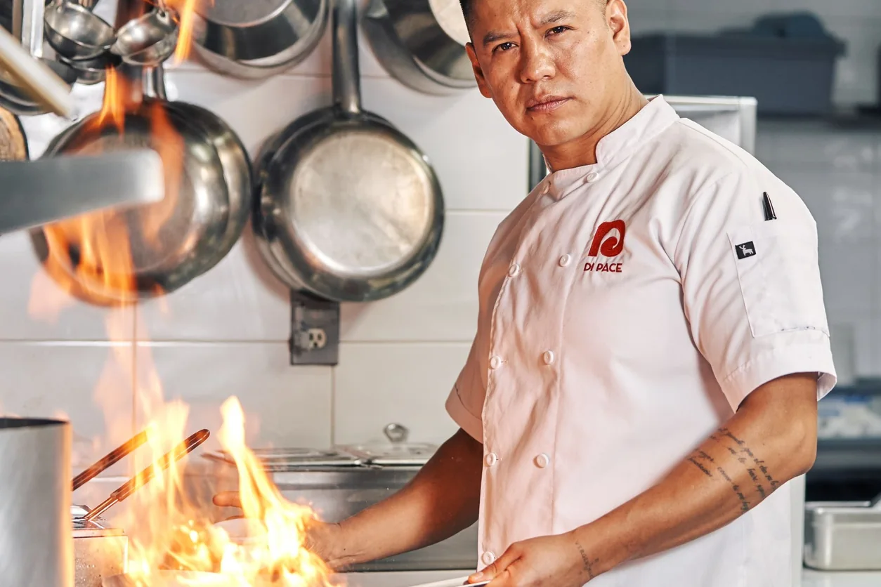 Chef expertly manages flames while cooking in a restaurant kitchen, showcasing culinary skills.