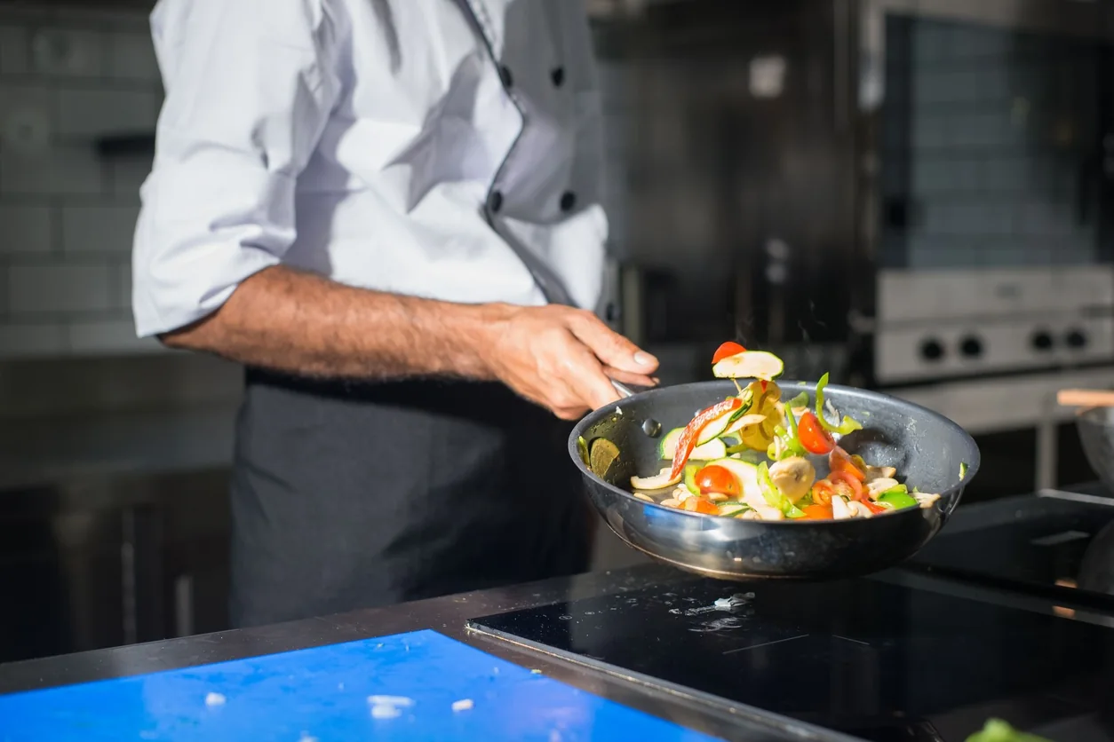 Professional chef tossing fresh vegetables in a frying pan in a modern kitchen.