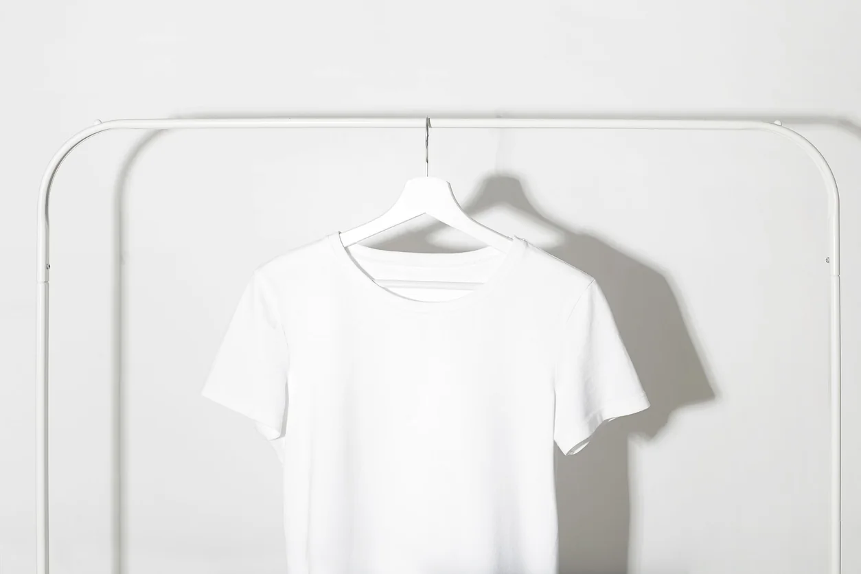 A white cotton T-shirt hangs on a clothes rail.