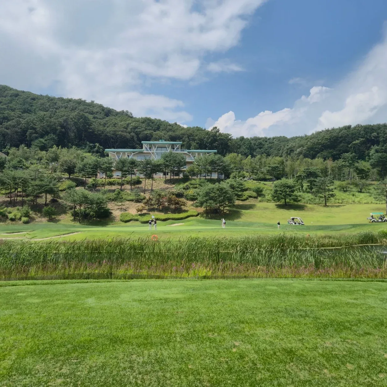 A picturesque golf course set against lush greenery and a modern clubhouse, under a vibrant sky.