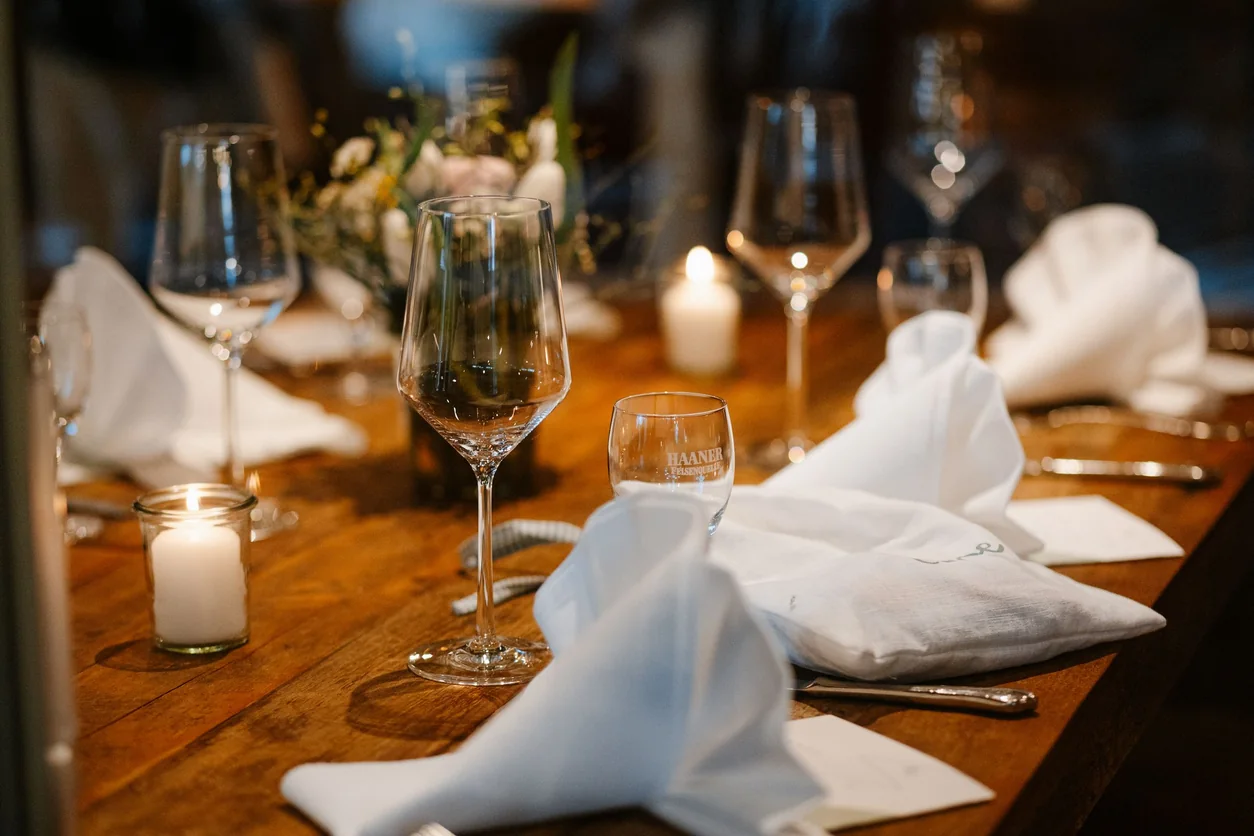 A candlelit restaurant table set with wine glasses, linen napkins and flowers.