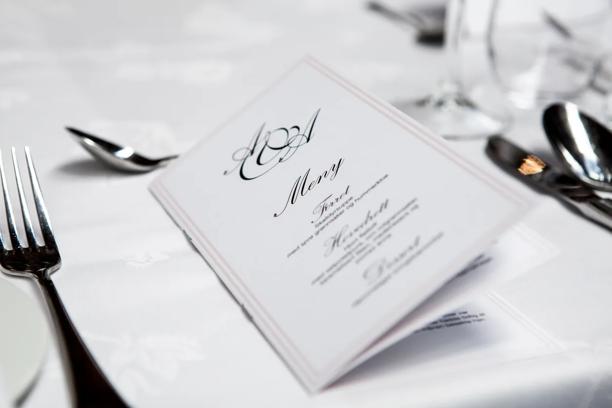 A printed menu on a white linen table beside polished cutlery and glassware.