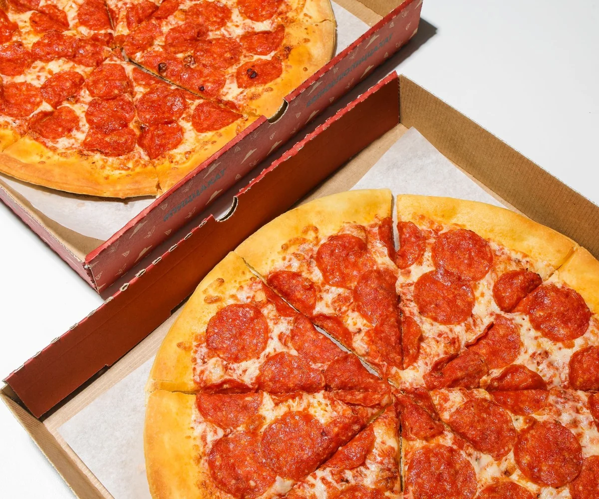 Top view of freshly baked pepperoni pizzas in open delivery boxes, ready to eat.