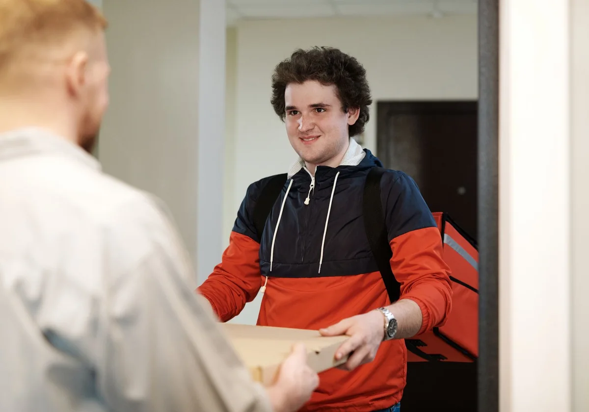 Pizza delivery man in casual wear delivers pizza box to a customer indoors, smiling