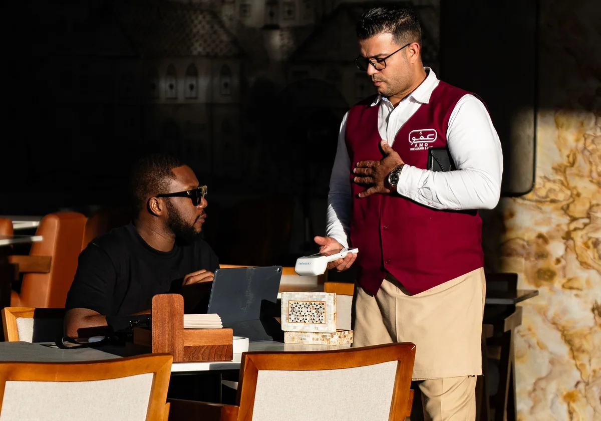 A waiter in uniform serves a customer in a trendy Dubai cafe with unique decor.
