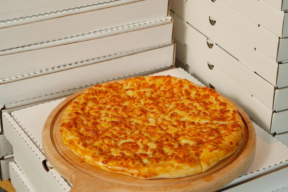 Appetizing cheese pizza on a wooden board atop a stack of delivery boxes, ready to serve.