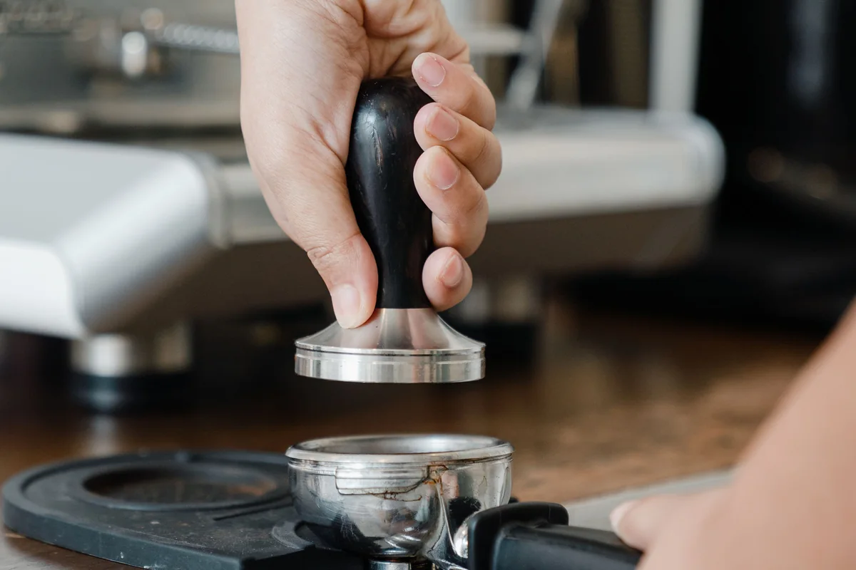 A close-up of a barista tamping espresso grounds.
