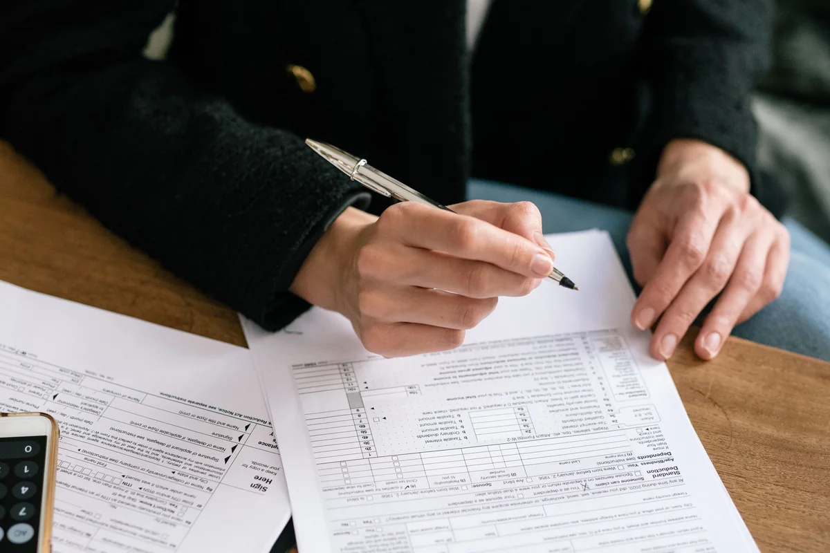 Hands reviewing paperwork with a pen at a wooden desk.