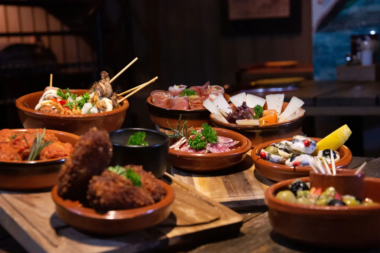 An assortment of tapas in terracotta bowls arranged across a wooden restaurant table.