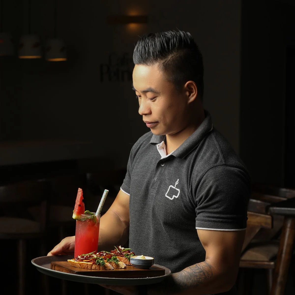 A server carrying plated food and a colorful drink through a warmly lit restaurant.