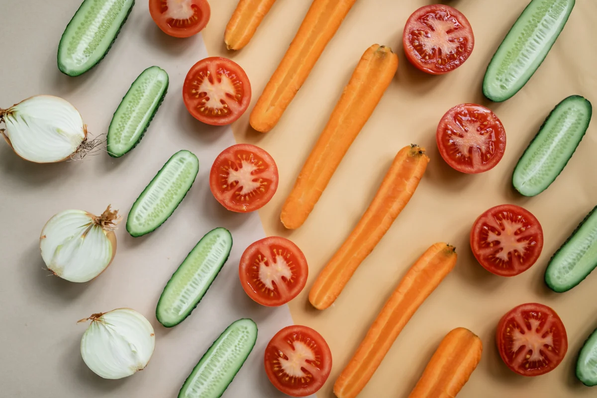Freshly sliced tomatoes, carrots, cucumber and onions arranged on a warm neutral background