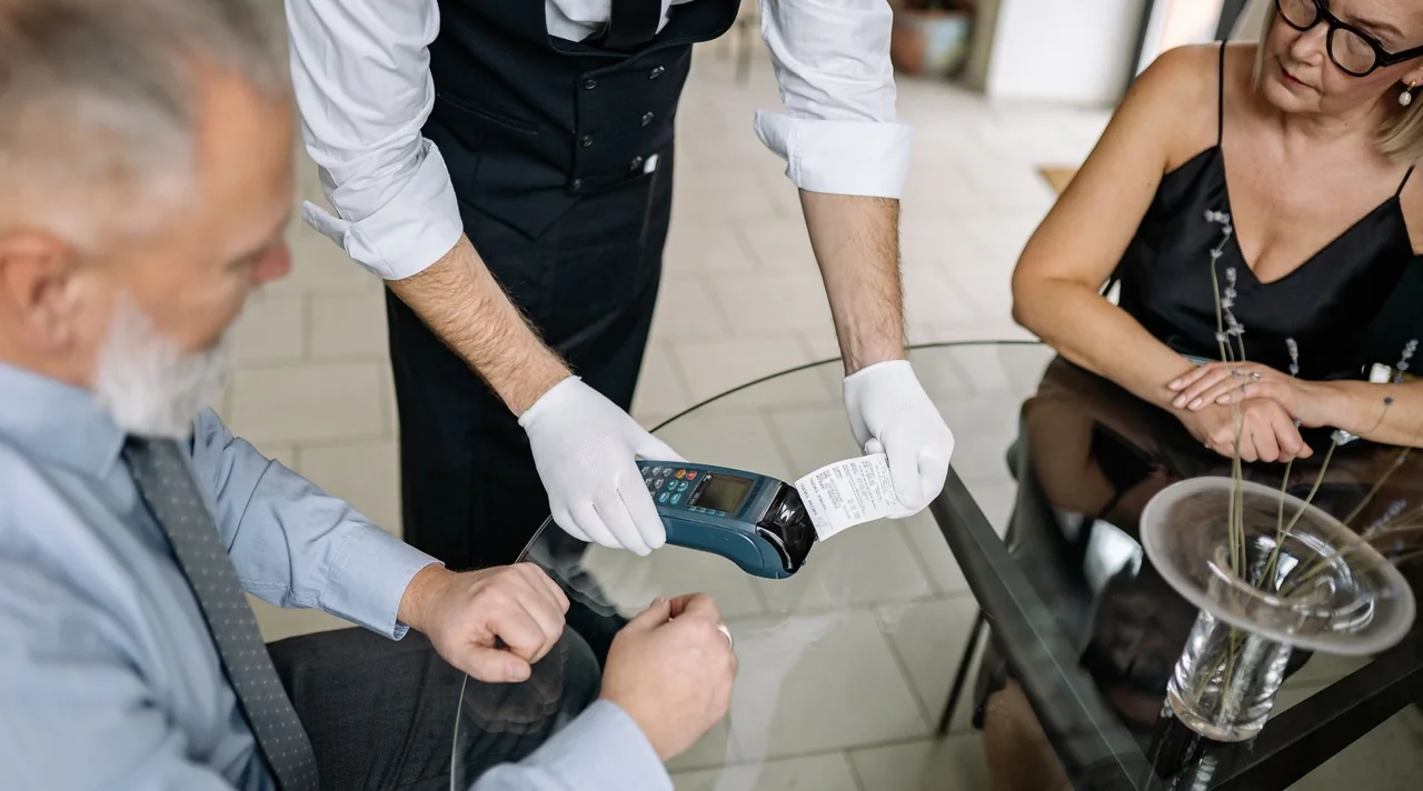 A restaurant guest holds a card over a handheld payment terminal.