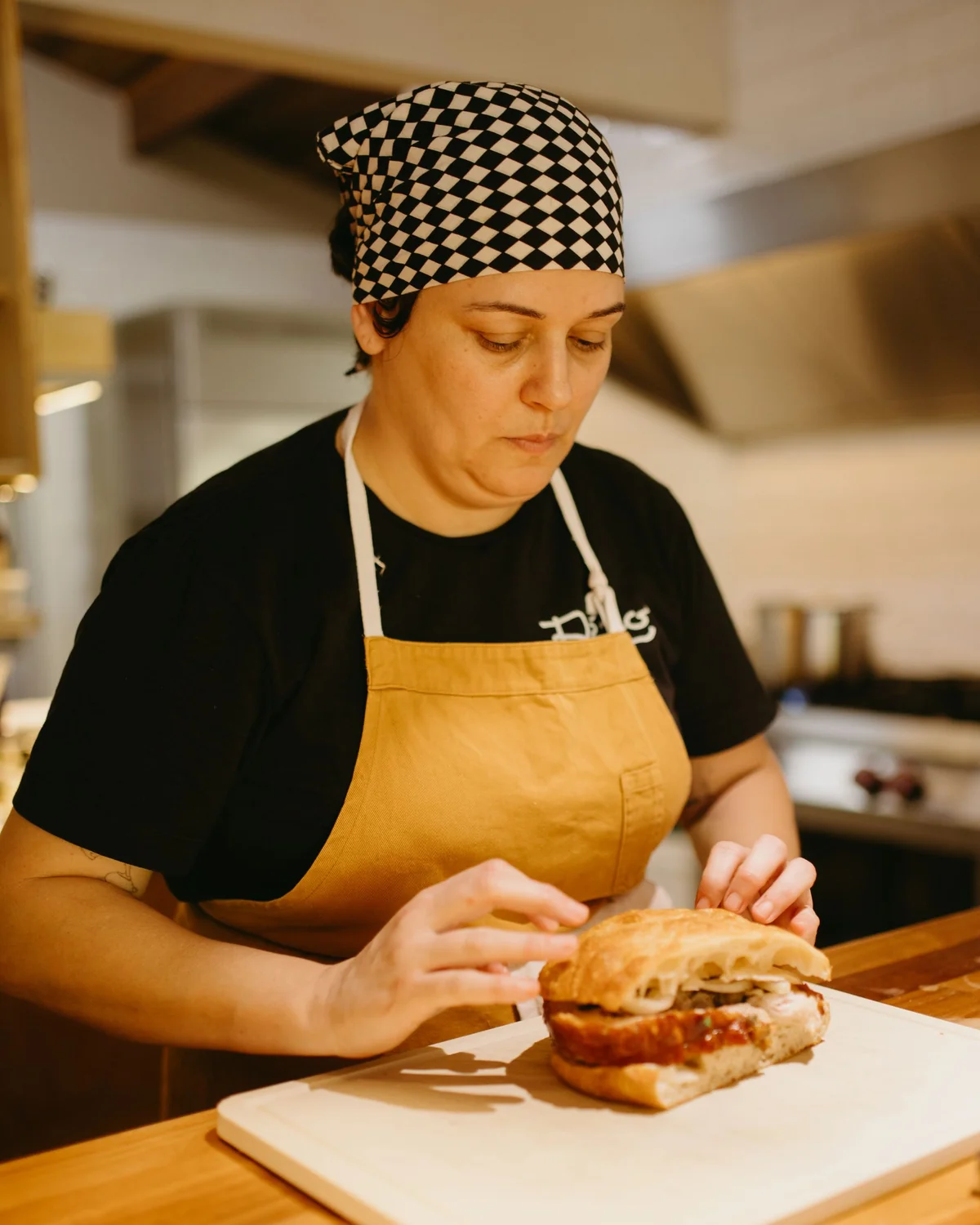 A chef in a golden apron preparing a sandwich in a warm restaurant kitchen.