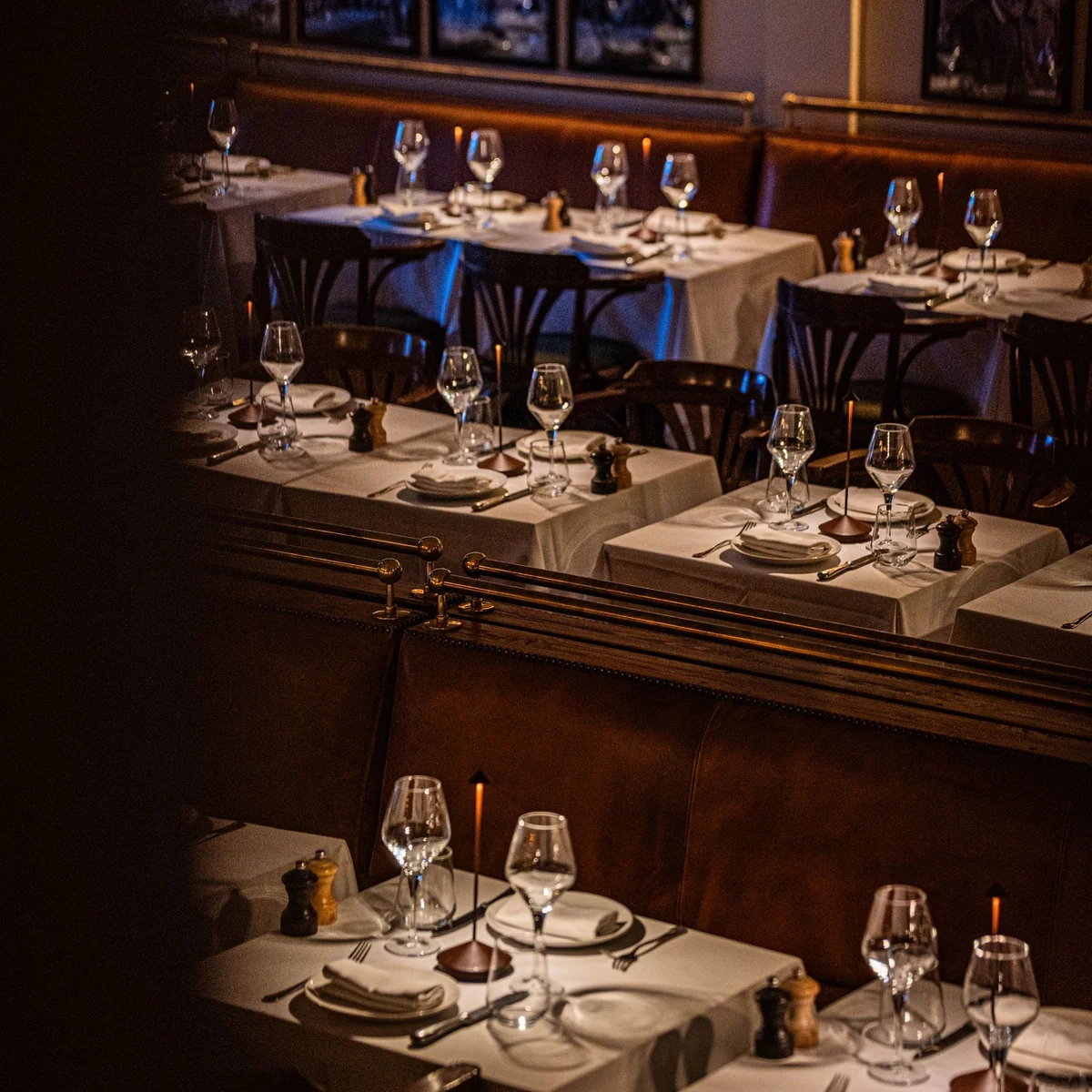 Tables set for evening service with white linen, glassware and warm wood details.