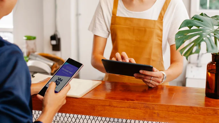 Hands using a tablet and phone at a cafe counter.