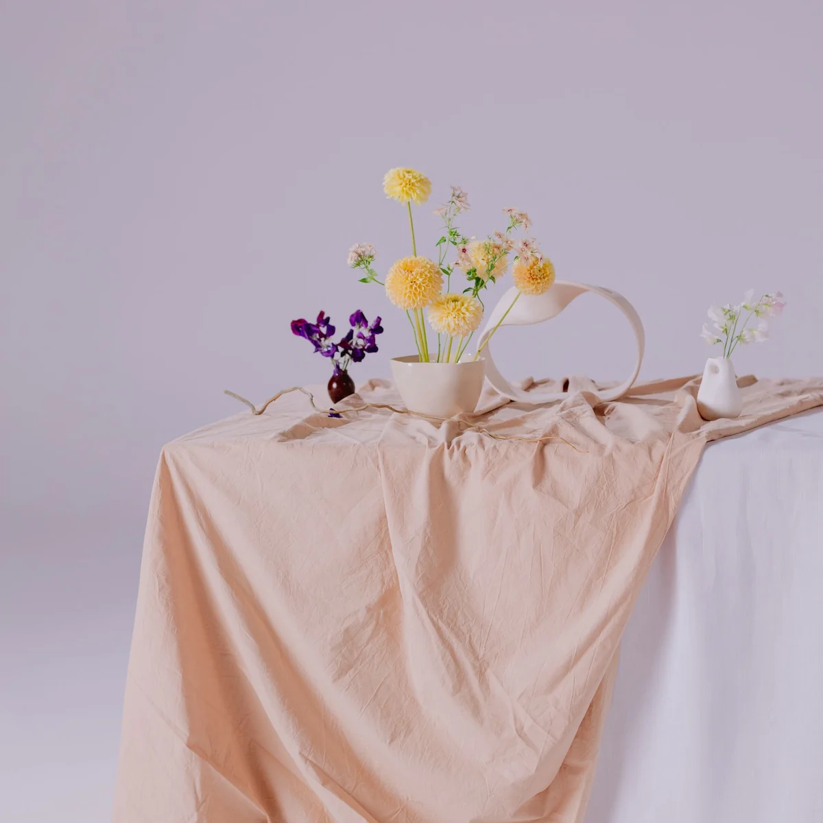 Flowers and sculptural ceramic vases arranged on peach fabric.