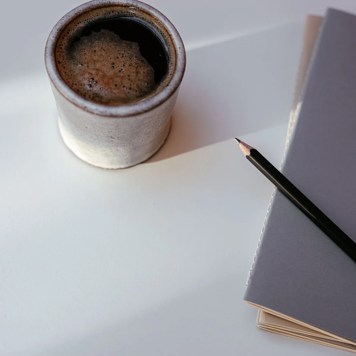 A ceramic coffee cup, pencil and notebook in natural light.