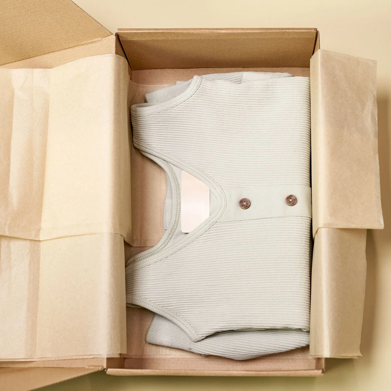 A ribbed cream top neatly folded in a tissue-lined cardboard box.